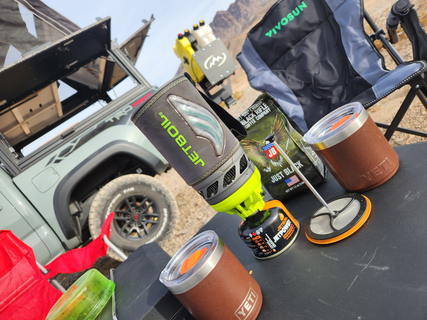 RV rental outdoor coffee break: Jetboil stove, Black Rifle Coffee, Yeti mugs, and an overland truck with a rooftop tent.