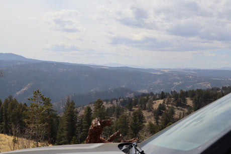 Scenic mountain vista from a car, ideal for an RV rental journey. Layered forests, hazy hills, and cloudy sky ahead.