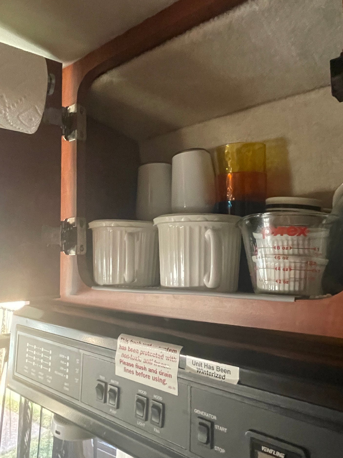 Inside an RV rental cabinet: winterized plumbing notice, kitchenware, and a control panel for generator & hood fan.