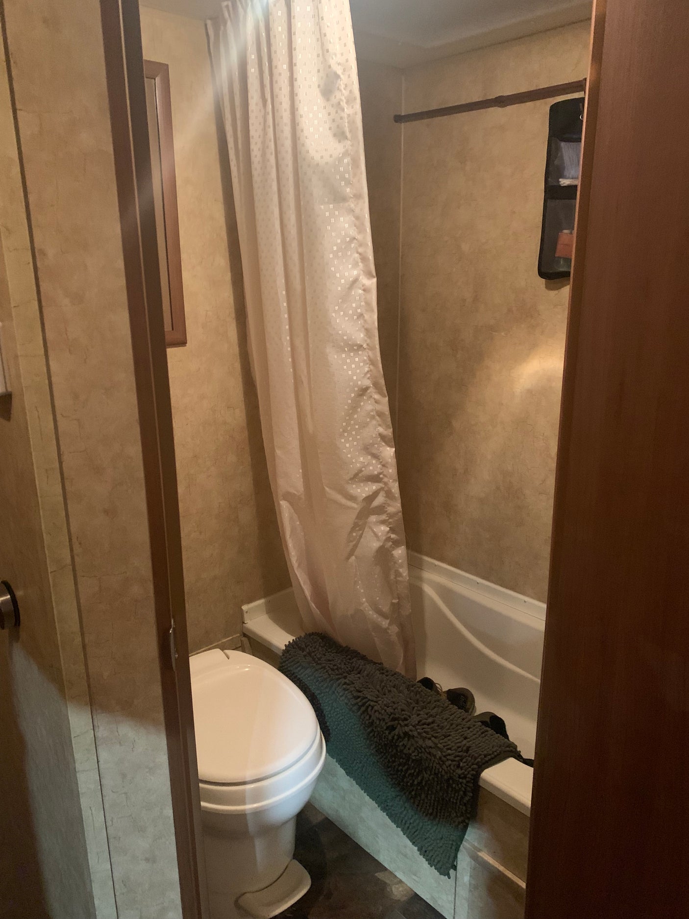 Compact bathroom in an RV rental, featuring a toilet, bathtub with shower curtain, and textured walls.