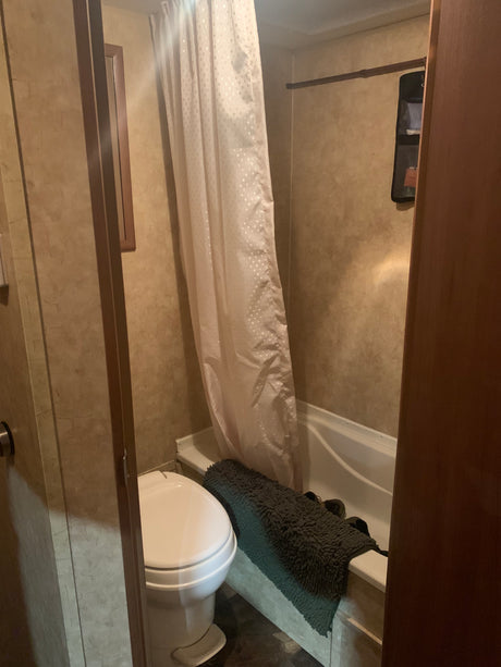 Compact bathroom in an RV rental, featuring a toilet, bathtub with shower curtain, and textured walls.