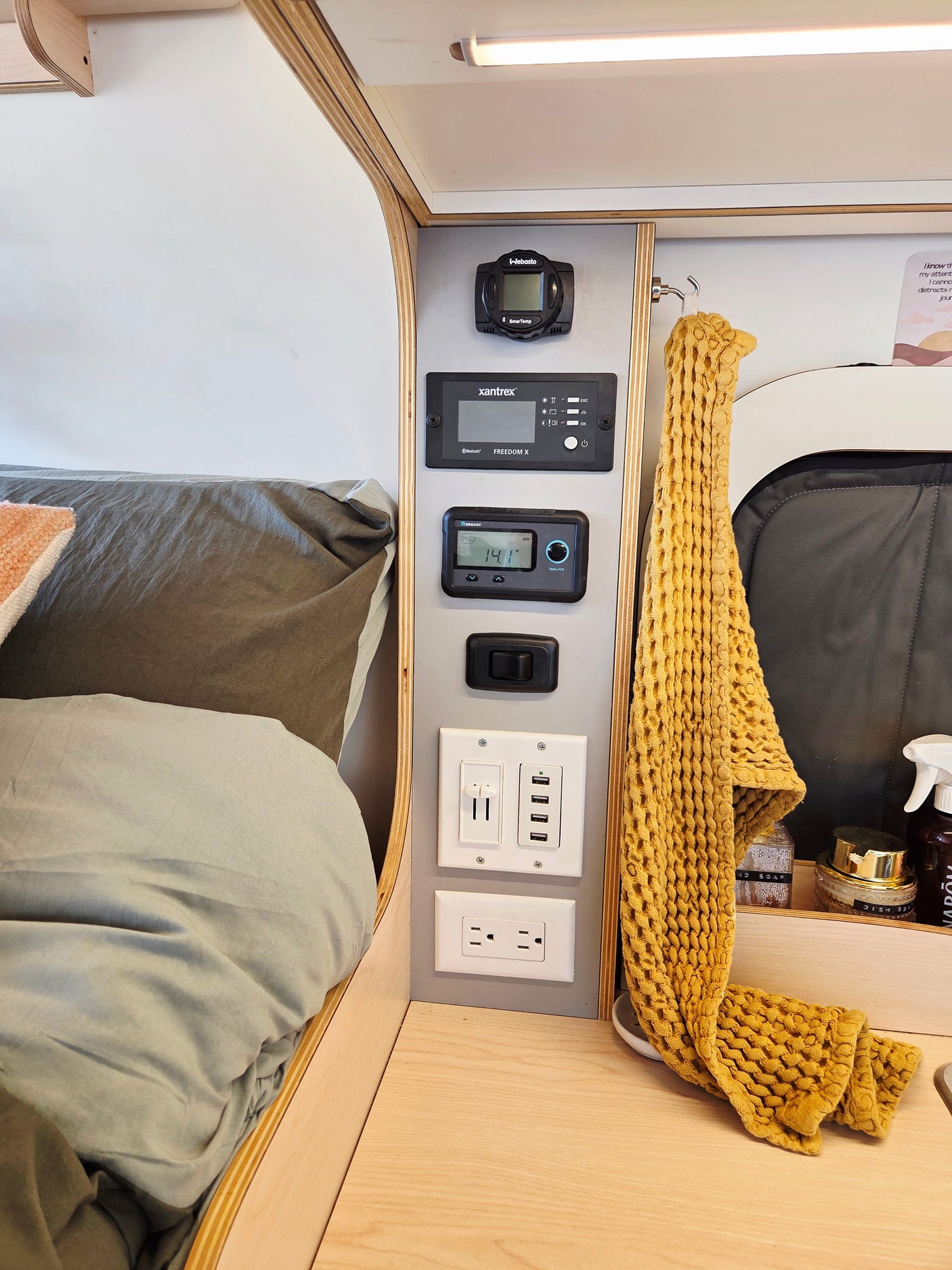 RV rental interior: bed, a multi-function control panel showing Webasto, Xantrex, Renogy, and various USB/AC charging ports.