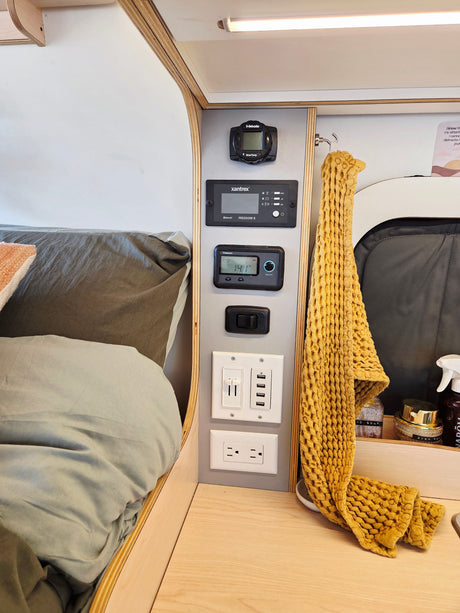 RV rental interior: bed, a multi-function control panel showing Webasto, Xantrex, Renogy, and various USB/AC charging ports.