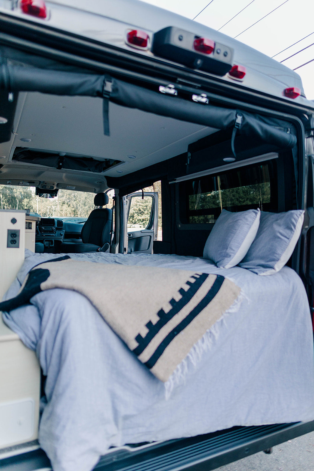 Inside an RV rental: a comfortable bed with light blue bedding and a patterned blanket, perfect for your next road trip.