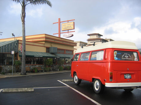 A red VW campervan, like an RV rental, is parked outside Giuseppe's Ristorante Italiano under a cloudy sky.