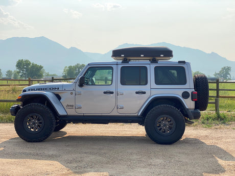 A silver Jeep Wrangler Rubicon with a roof box, ready for adventure. Perfect for an RV rental trip in the mountains.