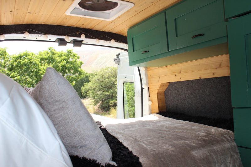 Cozy rv rental interior with a bed, green cabinets, and an open rear view of nature. — photo 8