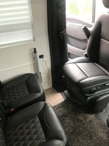 Cozy RV rental interior with black leather seats, a power outlet with a charging cable, and pleated window blinds.