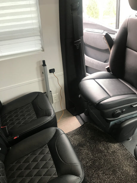 Cozy RV rental interior with black leather seats, a power outlet with a charging cable, and pleated window blinds.
