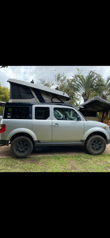 Silver Honda Element pop-top camper, ideal for rv rental adventures. Equipped with all-terrain tires for exploration.