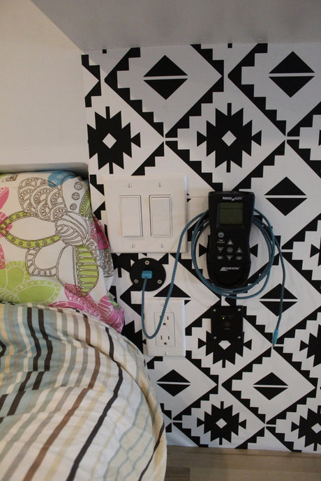 Convenient electrical setup in an rv rental, with outlets, light switches, and climate control remote on a patterned wall beside a bed.