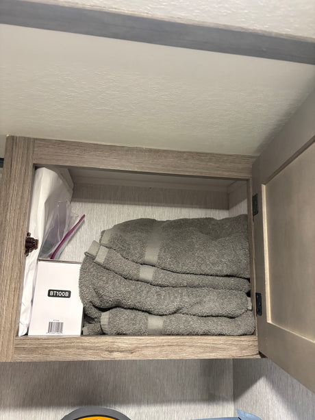 RV rental overhead cabinet: neatly folded grey towels & a box (BT100B) for organized storage in the RV interior.