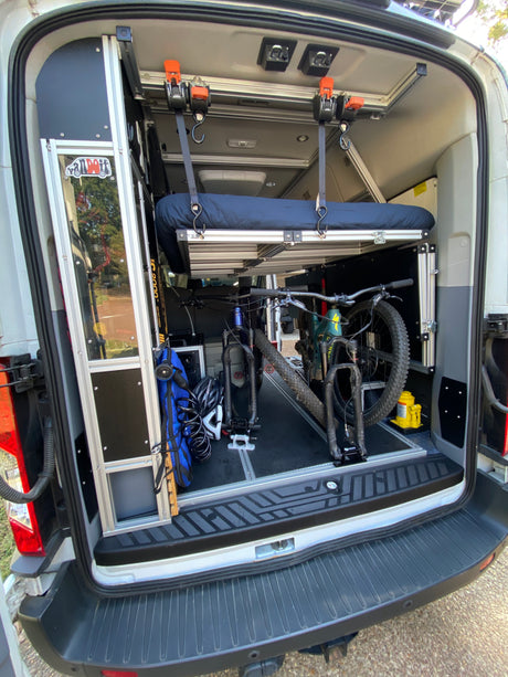 Inside an RV rental: custom camper van interior with elevated bed and two mountain bikes secured for travel.
