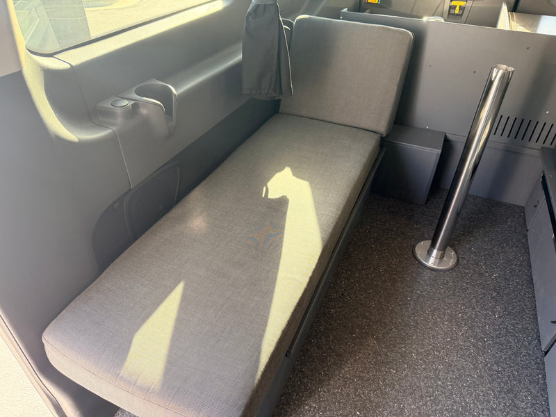 Interior of an RV rental: a sunlit, long gray bench seat, cup holder, and metal pole in a functional van conversion. — photo 14