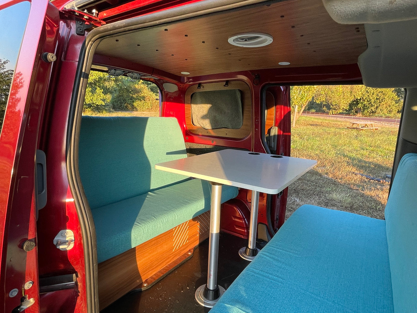 Cozy rv rental interior: A bright dining area with teal benches and a functional table, perfect for van life adventures.