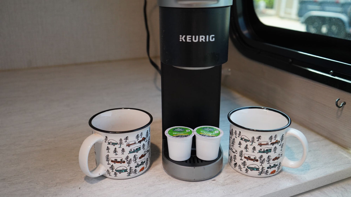 Enjoy morning coffee in your RV rental. Keurig machine, two K-cups, and two camping-themed mugs on the counter.