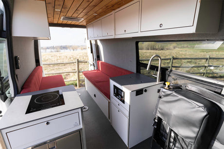 Spacious RV rental interior featuring a kitchenette with cooktop and sink, red bench seating, and wood ceiling.