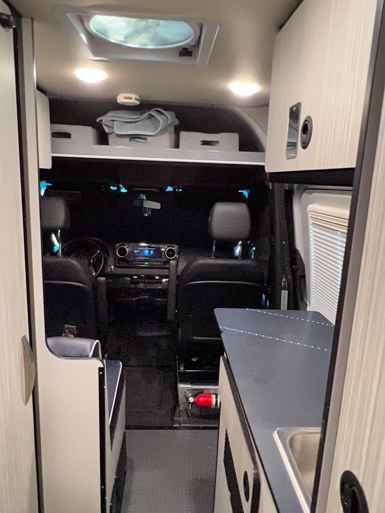 RV rental interior: A compact living space featuring a kitchen counter with sink on the right, an aisle, and front cabin.