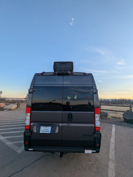 Rear of a dark Dazzle RV rental van, MO plate 07T93X. Parked facing a scenic vista at dusk, ready for adventure.