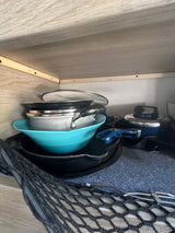 RV rental kitchen cabinet showcasing stacked pots, pans, and a colander, secured by a black mesh net. Compact cooking essentials storage.