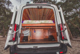Inside a custom-built camper van, featuring a cozy bed, ample storage, and plumbing, ideal for your next rv rental adventure.