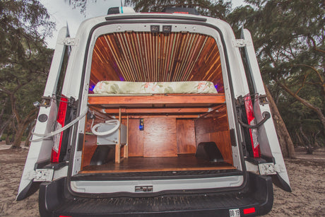 Inside a custom-built camper van, featuring a cozy bed, ample storage, and plumbing, ideal for your next rv rental adventure.