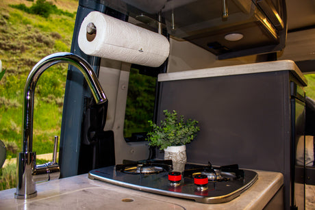 Inside a modern RV rental: a well-equipped compact kitchen with a faucet, two-burner stove, and paper towel holder.