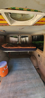 Inside an RV rental: a cozy elevated bed, ample floor space with a rug, and a ceiling fan for comfort.