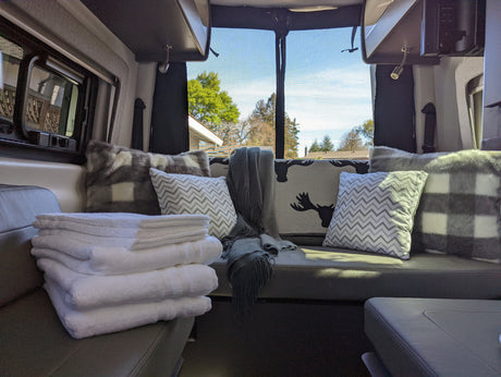 Comfortable RV rental interior featuring plush seating, white towels, and a scenic view through the large back window.