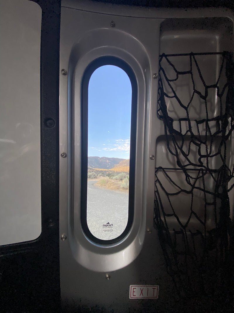 RV rental interior: oval window frames fall mountains, road. Storage nets & EXIT sign. — photo 15