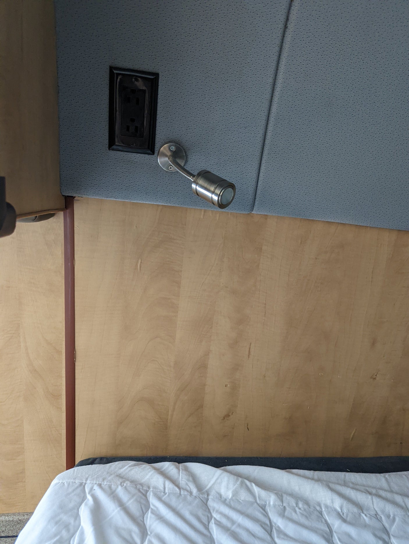 RV rental sleeping area: a wooden headboard, gray fabric panel with an outlet & flexible reading lamp.