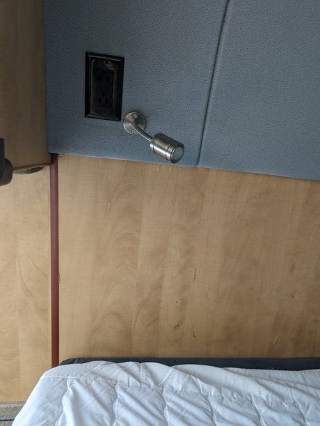 RV rental sleeping area: a wooden headboard, gray fabric panel with an outlet & flexible reading lamp.