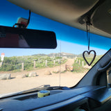 Inside an RV rental, looking out at a winding mountain road. A heart charm hangs, inviting scenic travel & adventure.