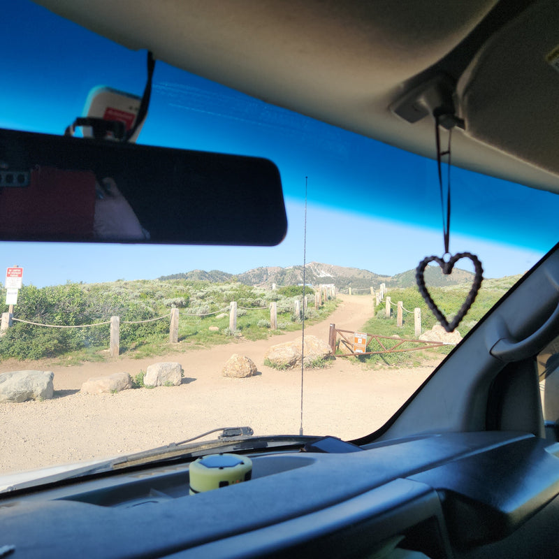 Inside an RV rental, looking out at a winding mountain road. A heart charm hangs, inviting scenic travel & adventure. — photo 8