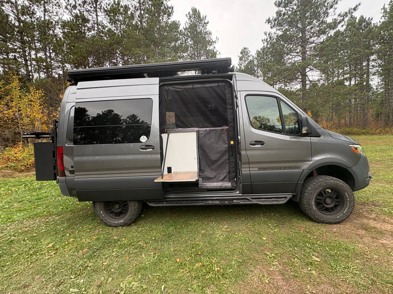  revealing interior. Features a roof awning and off-road tires.|RV rental camper van with an open door revealing a brown wood-grain fold-out table — photo 3