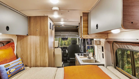 Inside an **RV rental**: a functional living space with bed, kitchenette, and overhead cabinets for your next road trip.
