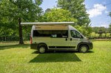 Parked on lush green grass, this gray RV rental offers an extended awning for comfortable outdoor adventures.