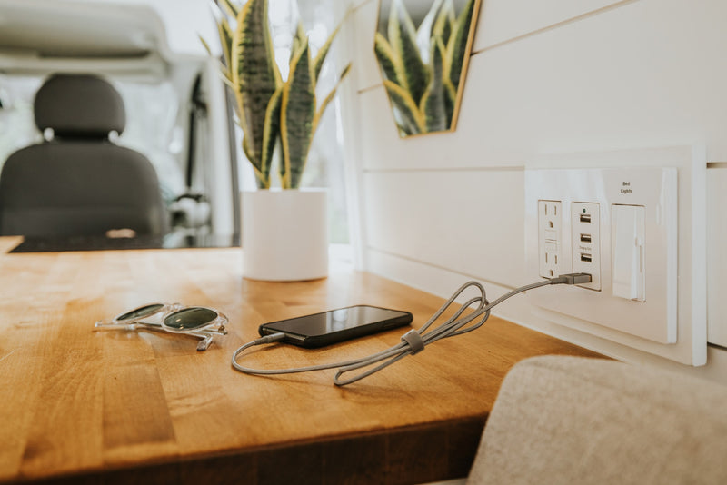 Stay powered on your RV rental adventure! Modern RV interior with a phone charging on a wooden counter, next to sunglasses & a plant. — photo 9