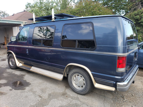 Dark blue conversion van, equipped with a roof rack and side steps, shown parked. Could be used as an RV rental.