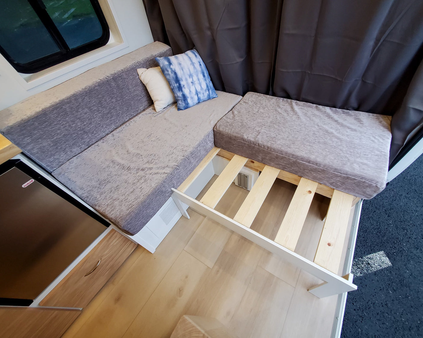 Versatile RV rental interior with L-shaped seating, pull-out bed frame, and built-in fridge for comfort.