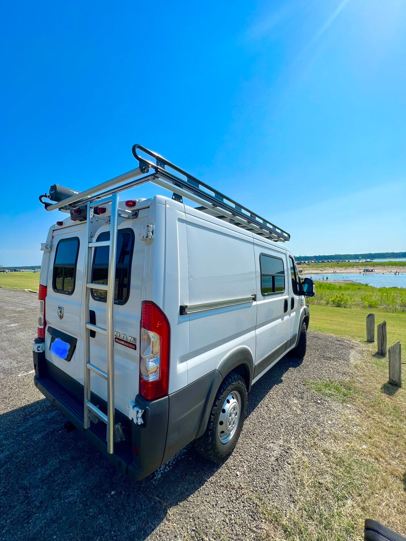 White RV rental camper van with a roof rack and ladder, parked lakeside on a sunny day, ready for outdoor adventures. — photo 13