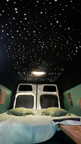 Enjoy this RV rental's custom interior: a dark ceiling with twinkling lights, comfy bed with green pillows, and unique wall panels.