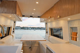 Spacious, modern RV rental interior with a cozy dining area & kitchen, featuring a beautiful waterfront view from open rear doors.