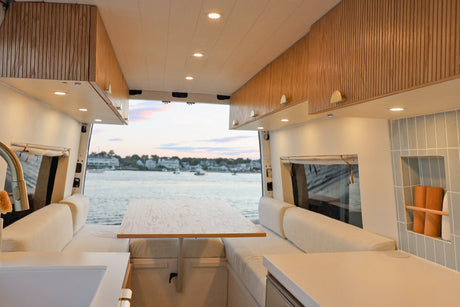 Spacious, modern RV rental interior with a cozy dining area & kitchen, featuring a beautiful waterfront view from open rear doors.