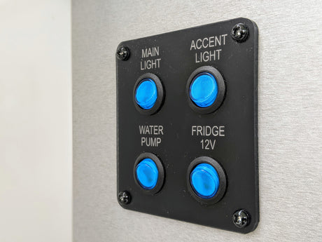 RV rental control panel featuring blue illuminated buttons for main light, accent light, water pump, and 12V fridge functions.