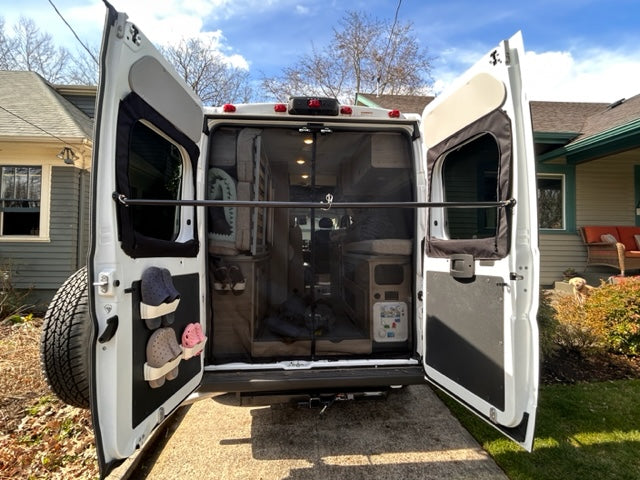 Open rear of an RV rental: mesh screen, interior with storage, and shoes organized on the left door. Ready for adventure!