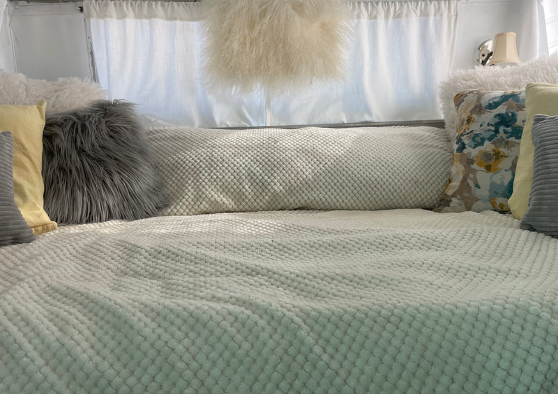 Cozy RV rental bed featuring textured white blankets, fluffy gray, white, and floral pillows. — photo 4