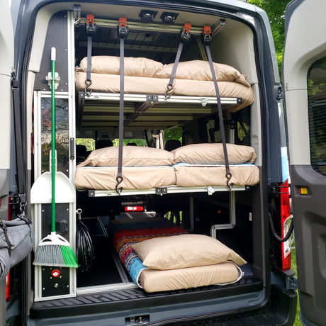 Inside an RV rental van: custom bunk beds for camping, neat storage for a broom & essentials.