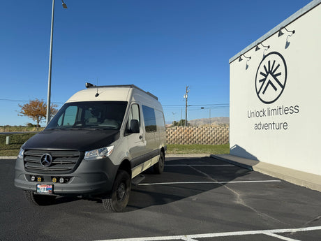 A custom Mercedes Sprinter van, an ideal rv rental, is parked near a white wall with "Unlock limitless adventure" text.