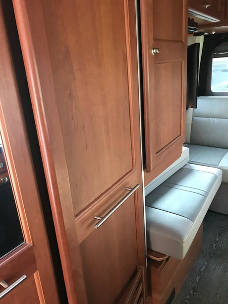 RV rental interior shows modern wood cabinetry, a tall refrigerator, and a light gray bench seat for comfortable travel.